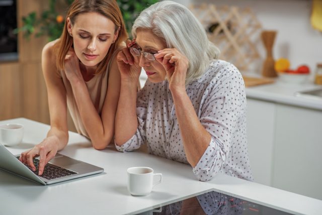 A mother and daughter look at a laptop. The daughter is helping her mother.