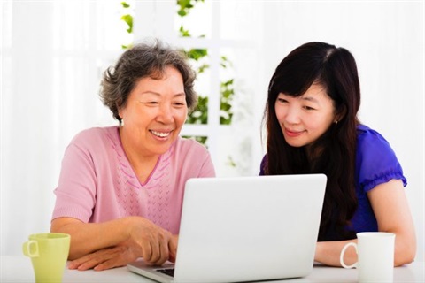 An older woman and her daughter looking at a laptop while smiling.